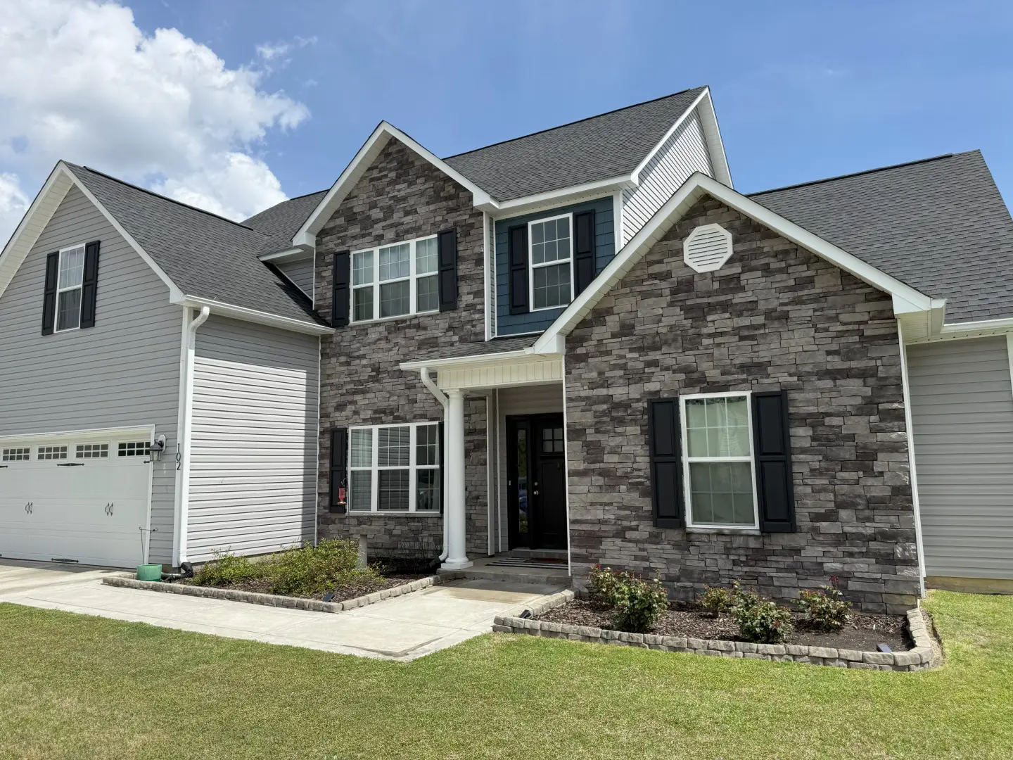Pressure washing cleans the stone and siding of a home, revealing a vibrant and well-maintained exterior.
