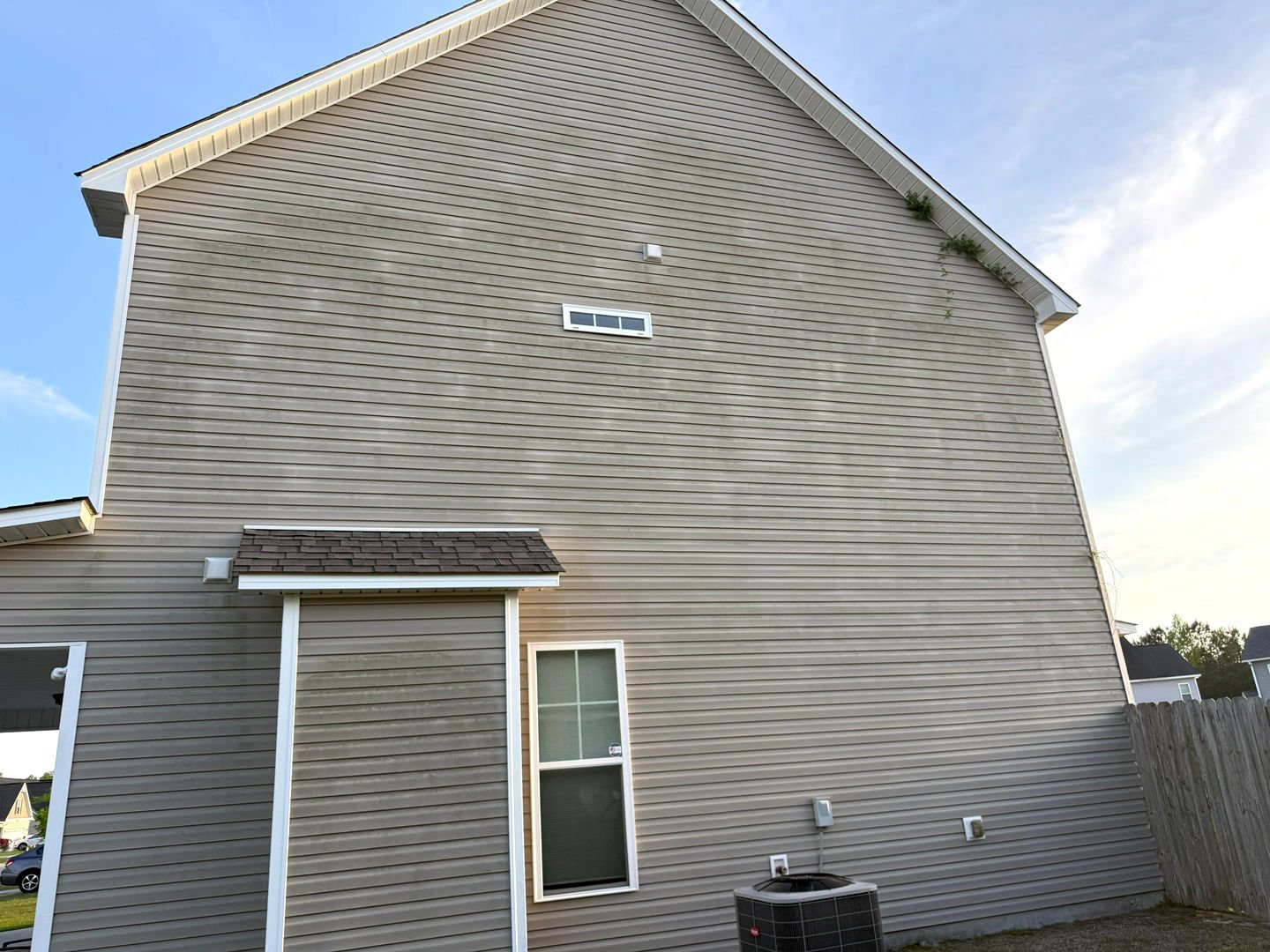 Pressure washing a home's vinyl siding, showcasing significant cleanliness improvement with dirt and grime removed.