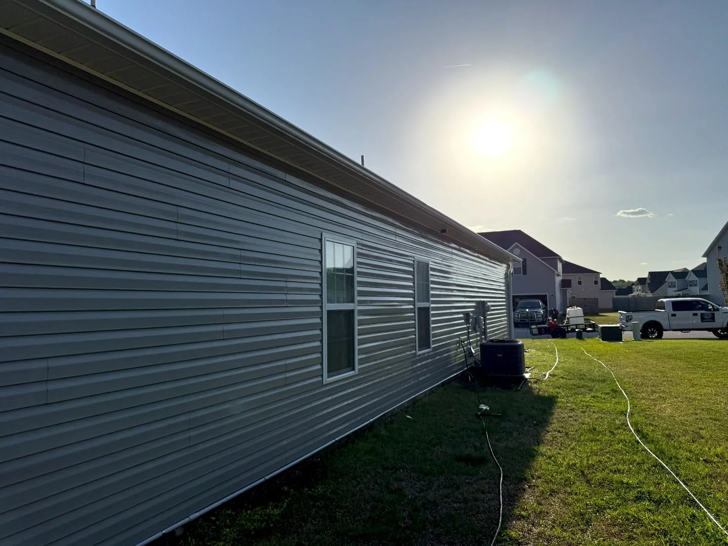 Pressure washing a vinyl house exterior, revealing a clean, bright surface free of dirt and grime under the afternoon sunlight.