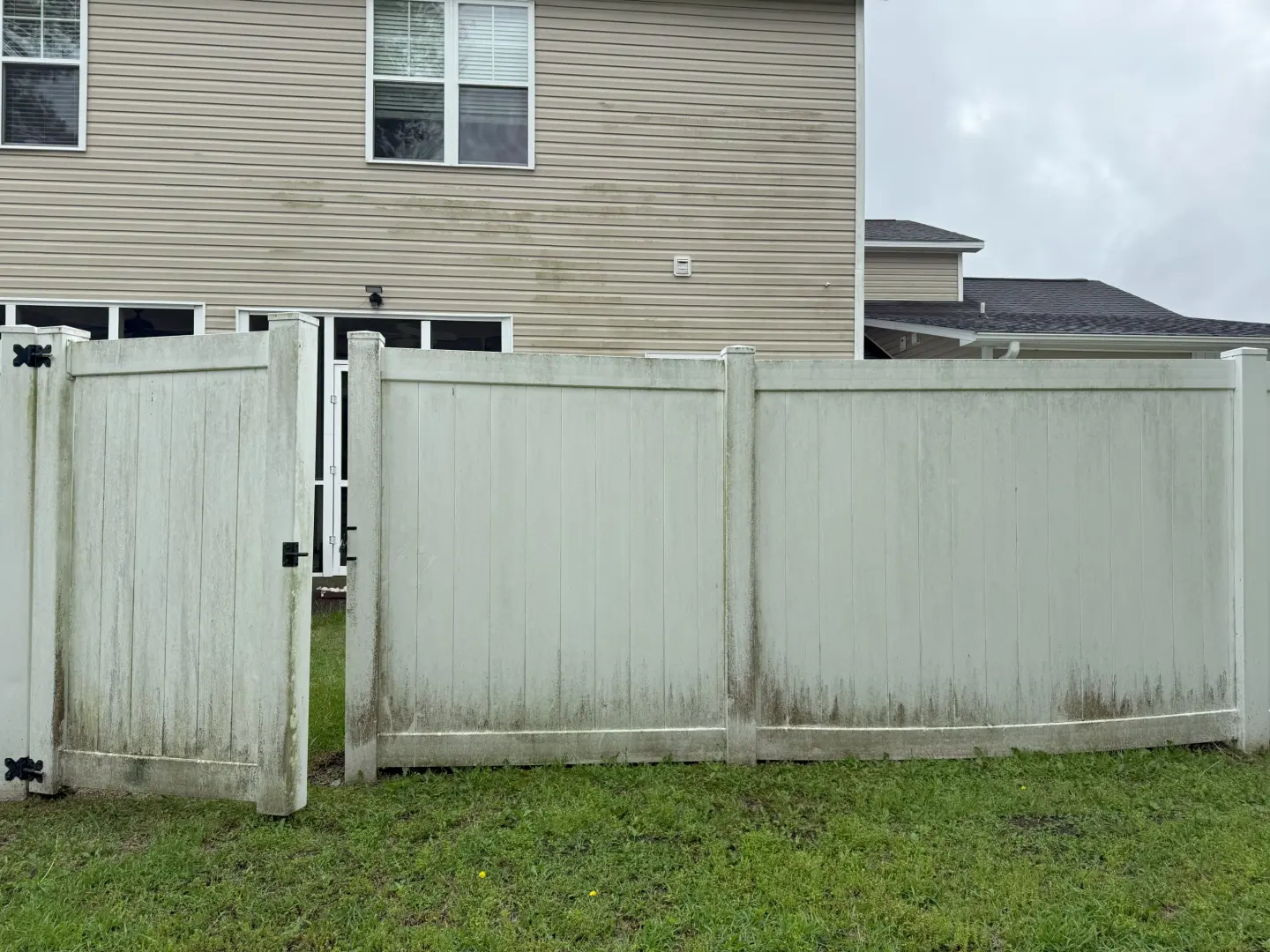Before and after pressure washing a dirty white vinyl fence, showing significant dirt removal and restoration.