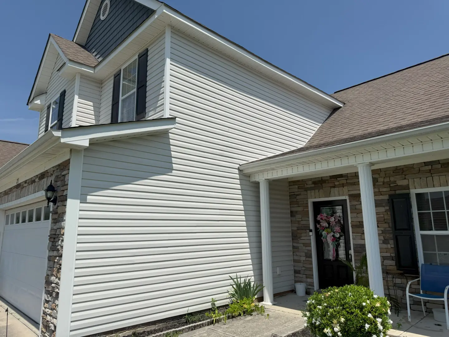 Pressure washing removes dirt and grime from a residential vinyl siding, enhancing its bright and clean appearance.