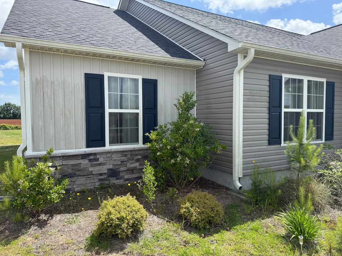 Pressure washing removes grime from the side of a house, showcasing a dramatic before-and-after cleaning effect.