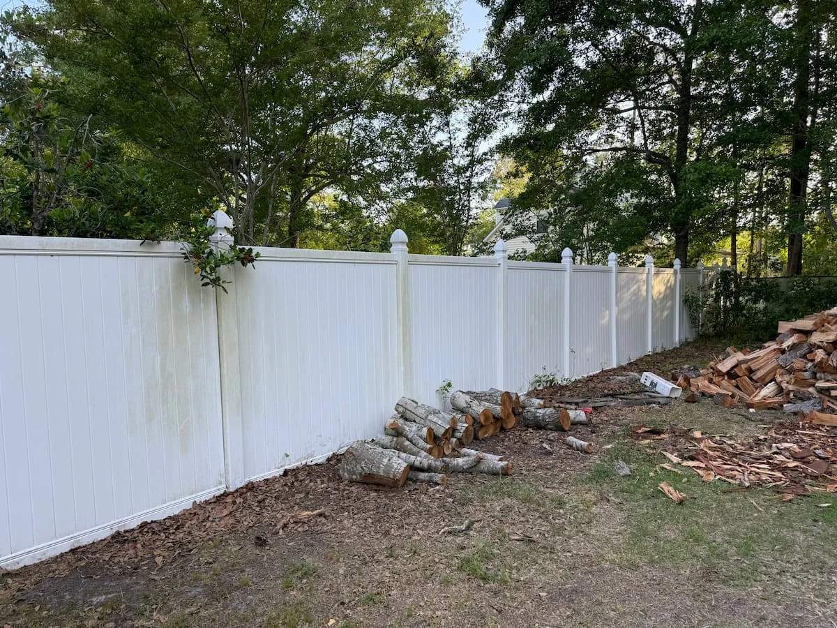 Cleaned white vinyl fence shows significant removal of dirt and mildew, enhancing curb appeal in garden area.